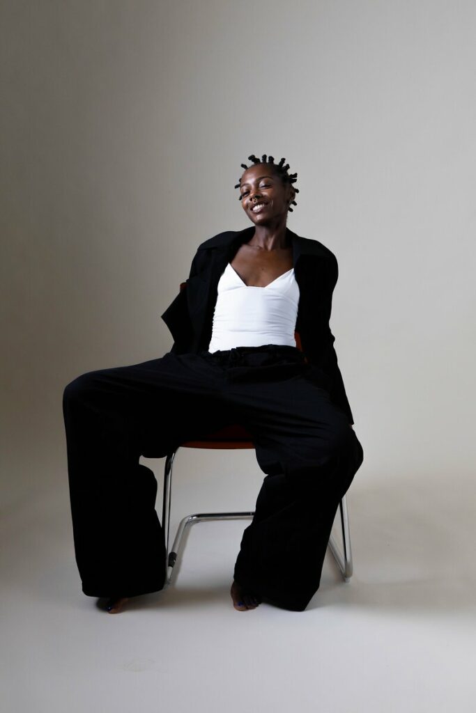 Shooting mode : mannequin en tailleur noir assise sur une chaise, fond gris au studio Muze à Ivry-sur-Seine