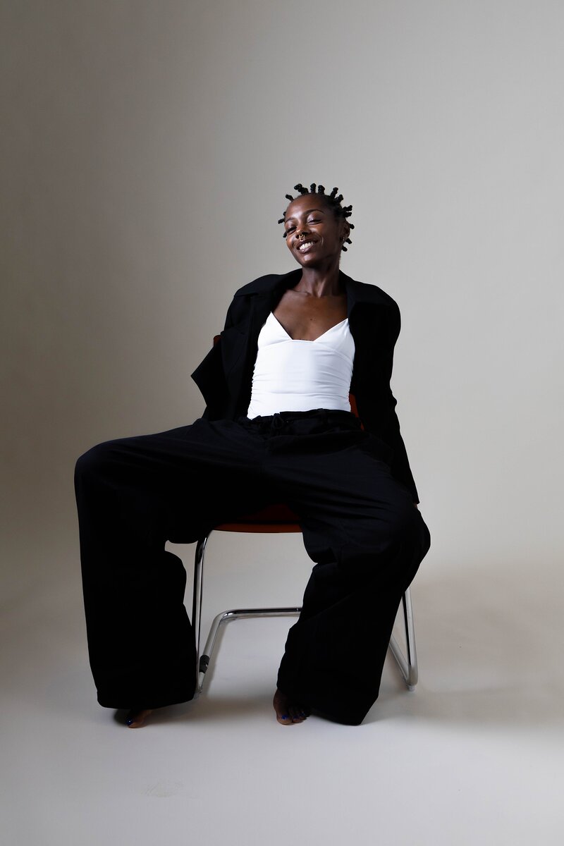 Shooting mode : mannequin en tailleur noir assise sur une chaise, fond gris au studio Muze à Ivry-sur-Seine