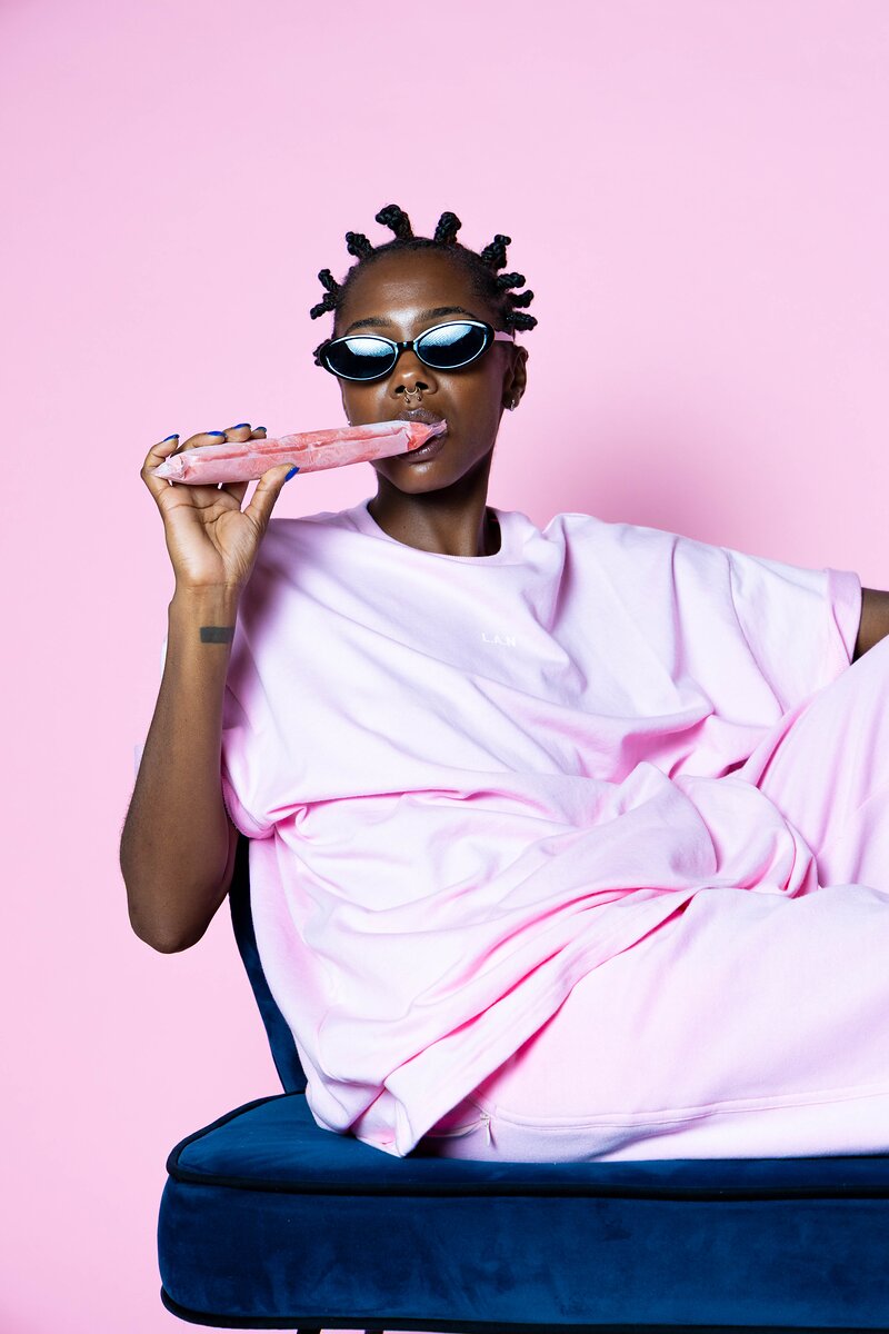 Shooting mode : mannequin souriante en t-shirt rose et lunettes noires sur un fauteuil bleu au studio Muze à Ivry-sur-Seine